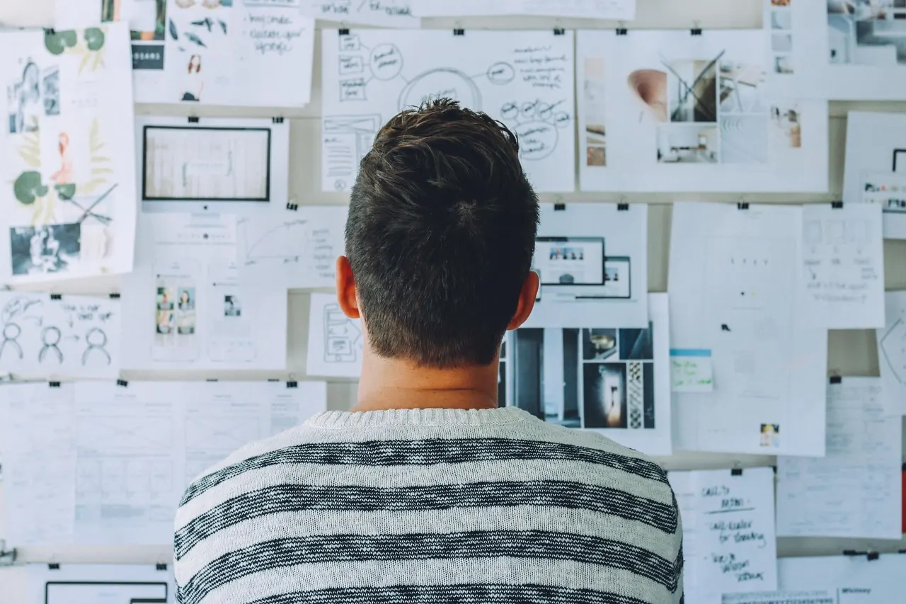 Person reviewing a wall of research notes and mockups while planning a competitor analysis